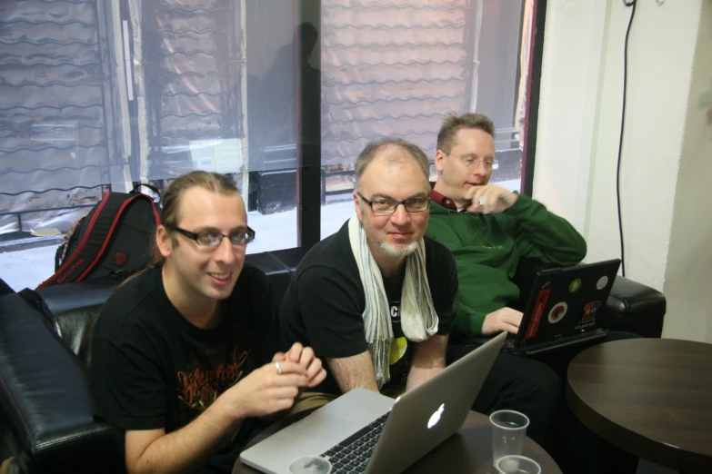 three men on a laptop and smiling at the camera