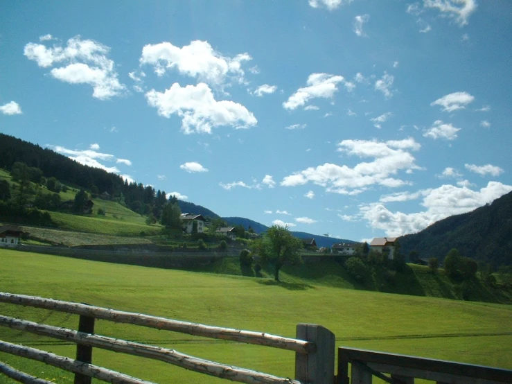 the view of a large grassy field from behind a wooden fence