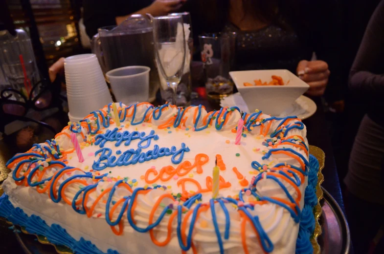 a birthday cake that is white with blue, orange and yellow frosting