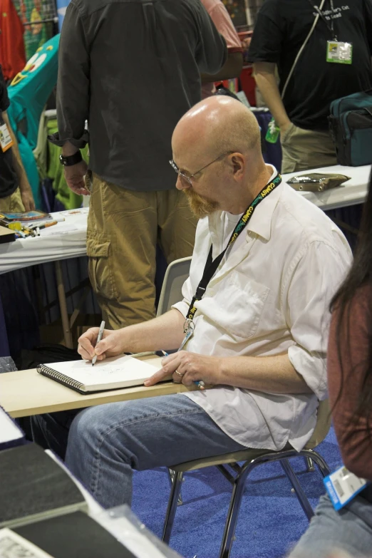 a man with a pen sitting at a table while writing on paper