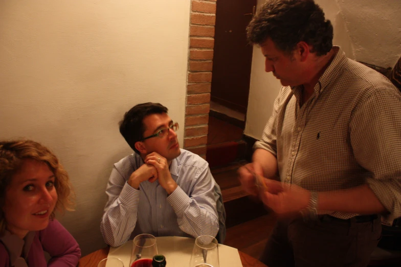 three people sitting at a table with two of them holding their hands over their mouths