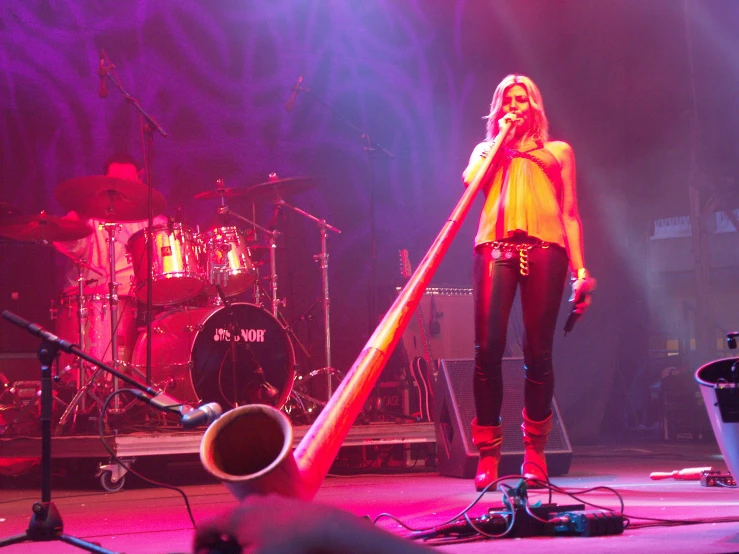 woman in yellow top holding up giant wooden instrument
