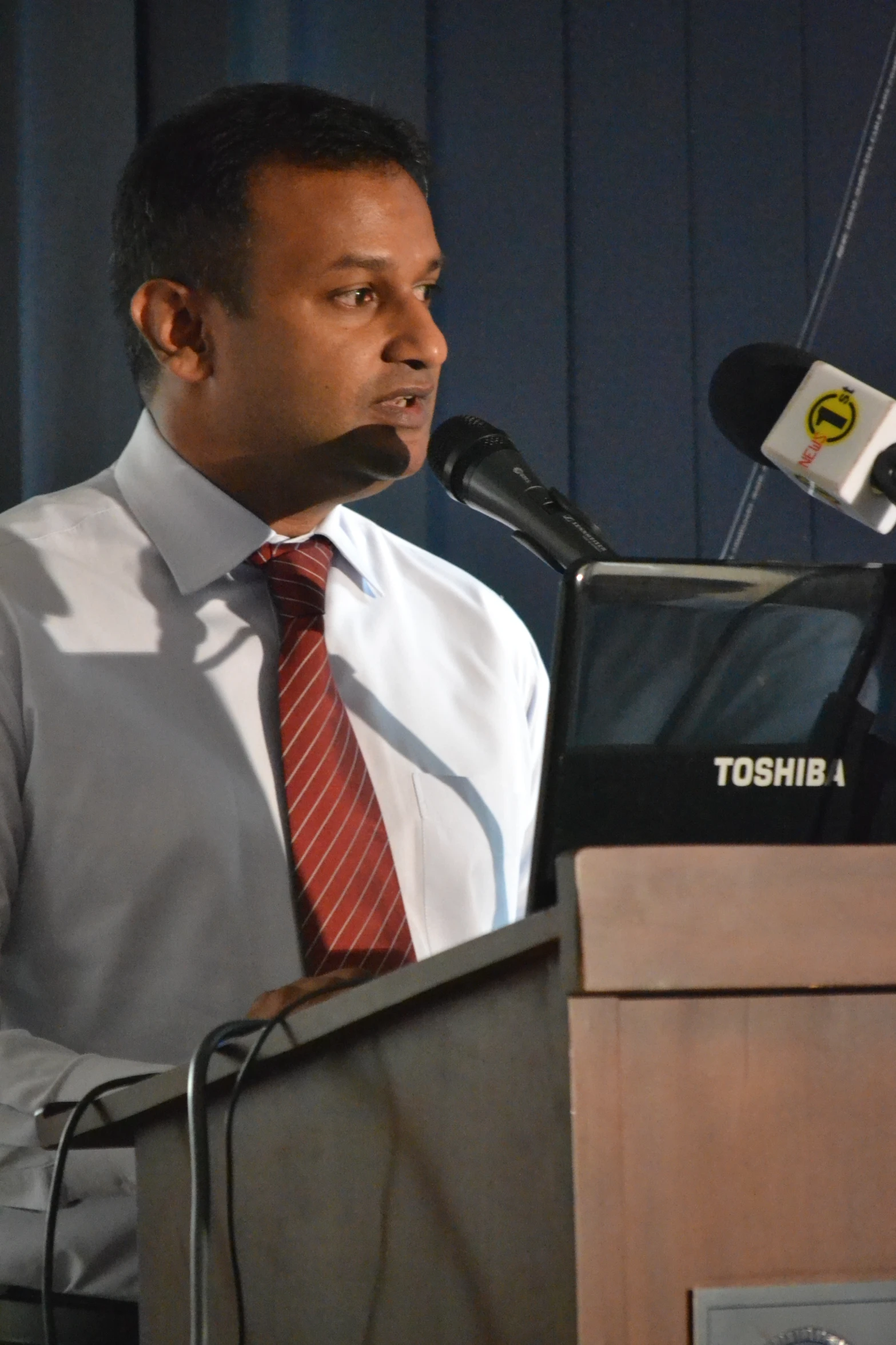 a man wearing a tie and a white dress shirt stands at a podium and speaks