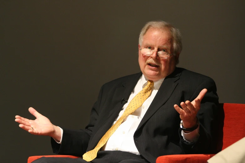 an older man with glasses talking at a meeting