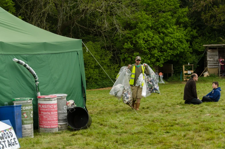 people are sitting in the grass near a large green tent