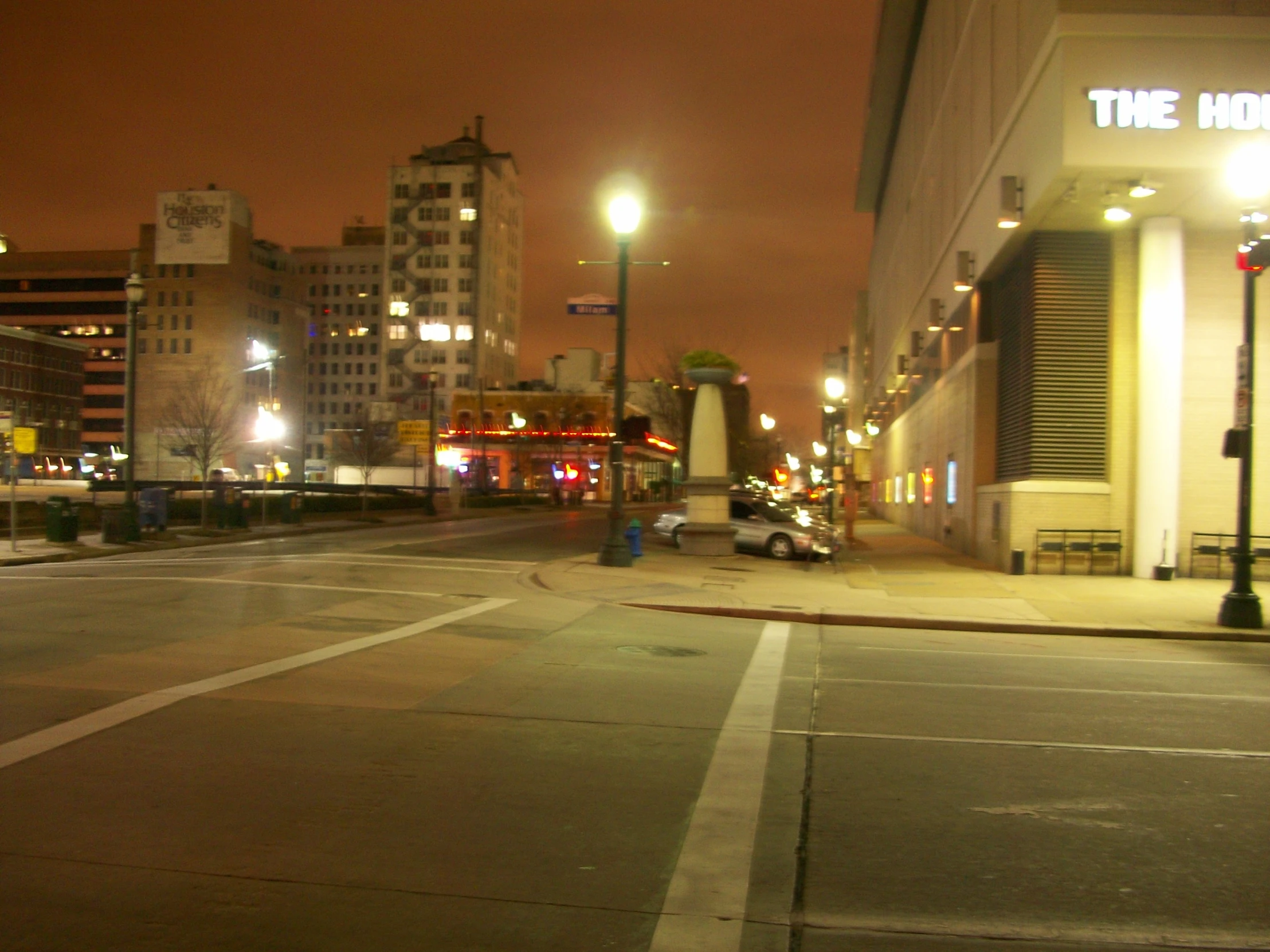 an empty city street with a couple cars parked at the corner