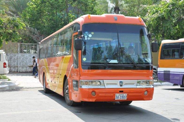 an orange bus stopped in a parking lot with other buses