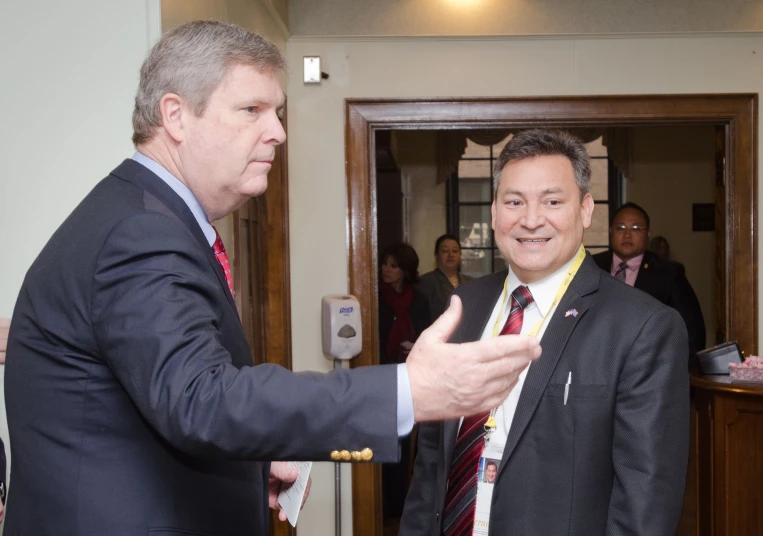 two men standing next to each other talking in front of a group