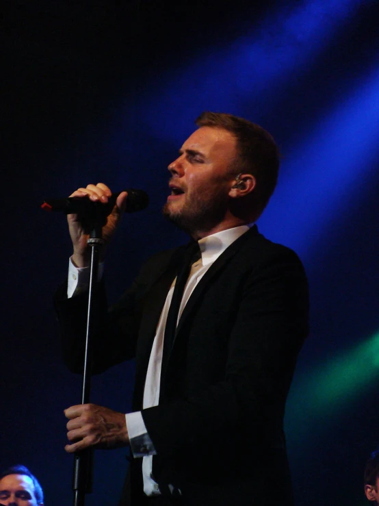 man in black suit holding microphone while performing on stage