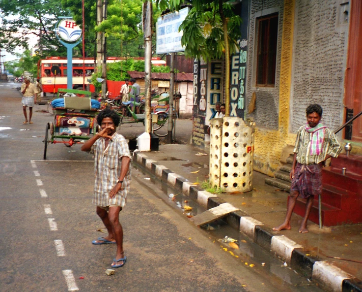 two boys on the street with one standing, holding a pole, and another walking