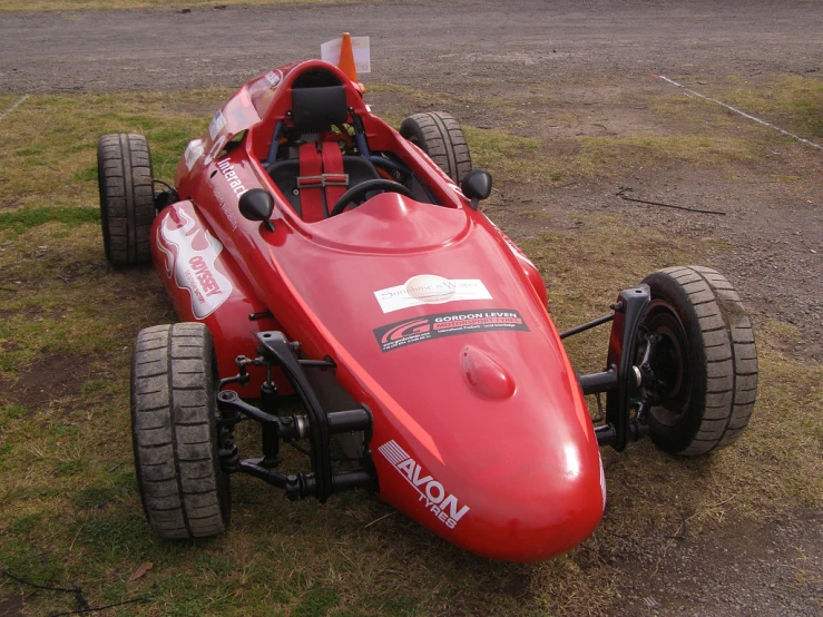 a red race car sits parked on some dirt