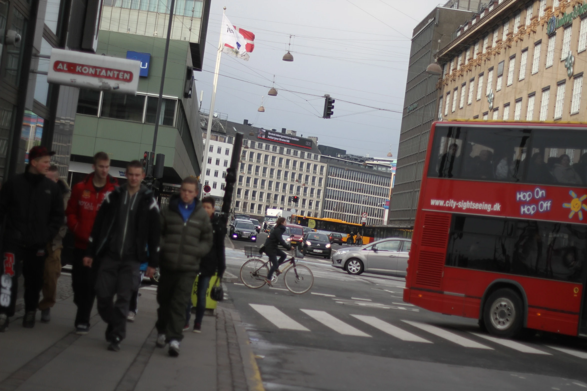 pedestrians walk down a busy street as buses and bicycle riders pass