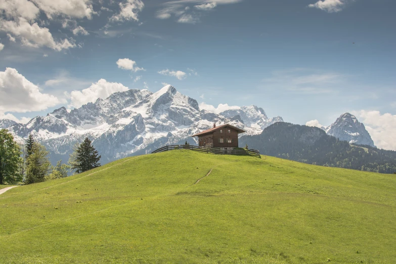 a hut on a green hill with mountains in the background