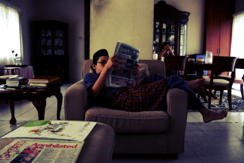 a man reads the paper while laying on his couch