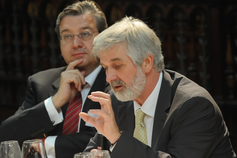 two men sit next to each other in front of wine glasses