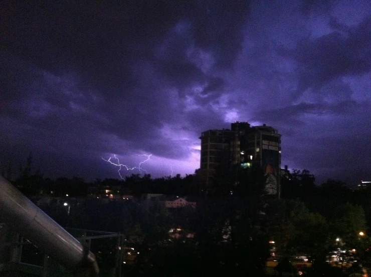 a lightning strike is seen from a rooftop during a dark sky