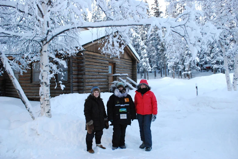 three people are standing in the snow outside a cabin