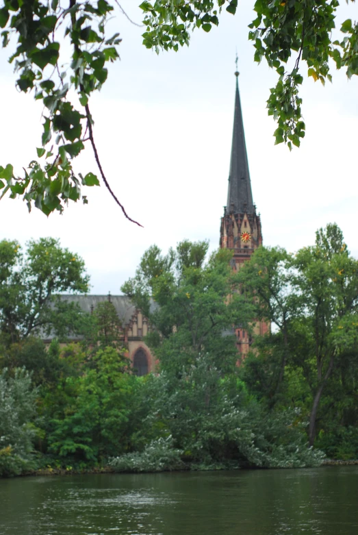 trees in the foreground of an old building on a lake with trees near by