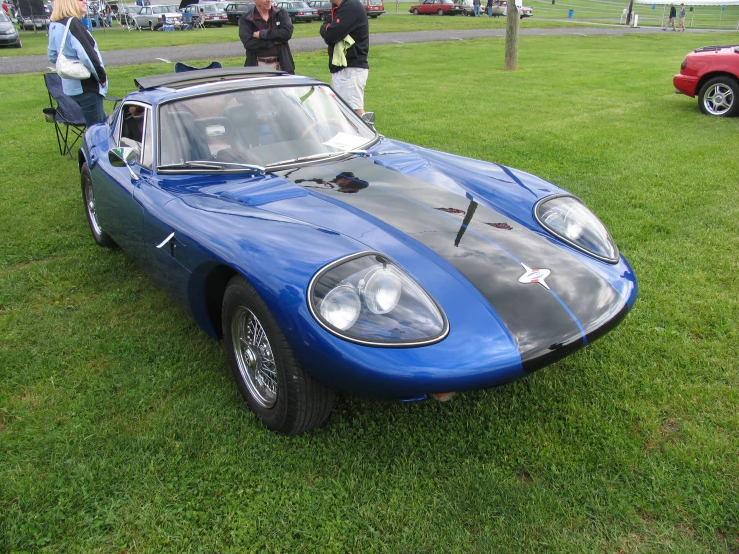 people talking near an old blue sports car