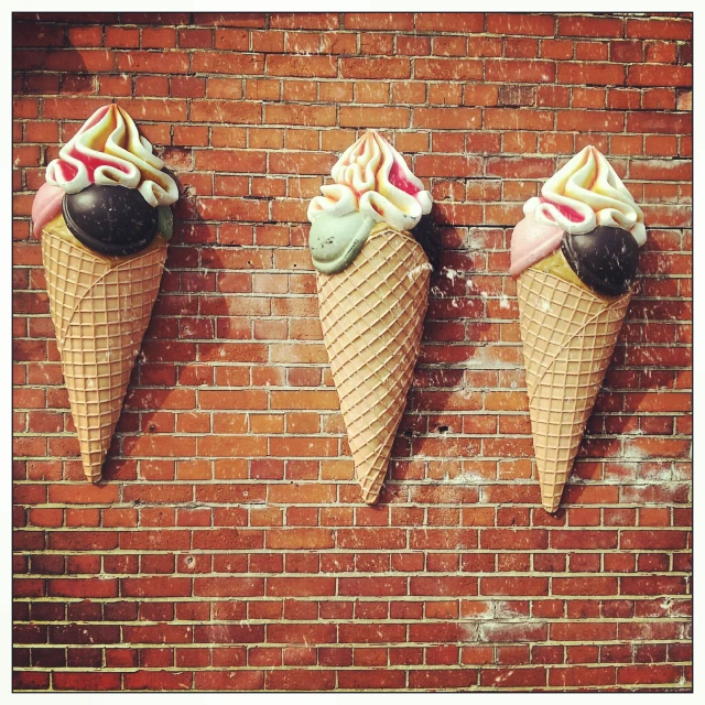 three ice cream cones that are hanging from a brick wall