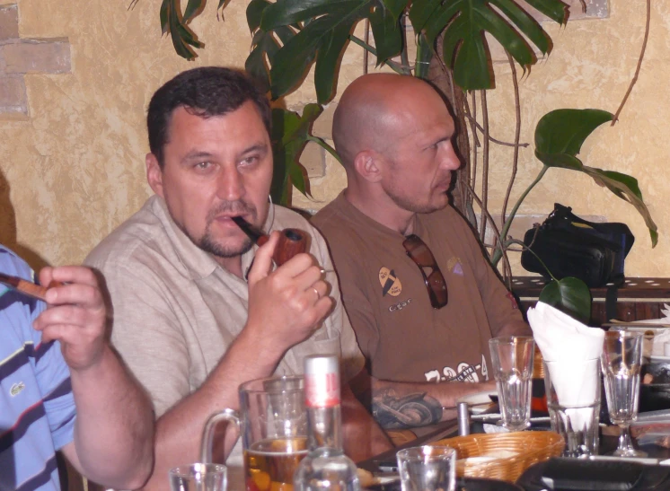 two men sitting at a table holding beverages