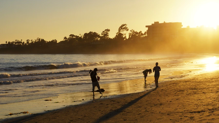 four people walking on the beach next to water and buildings