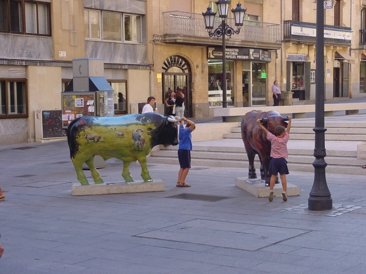 people pographing statues with a cow and other animals on a city street