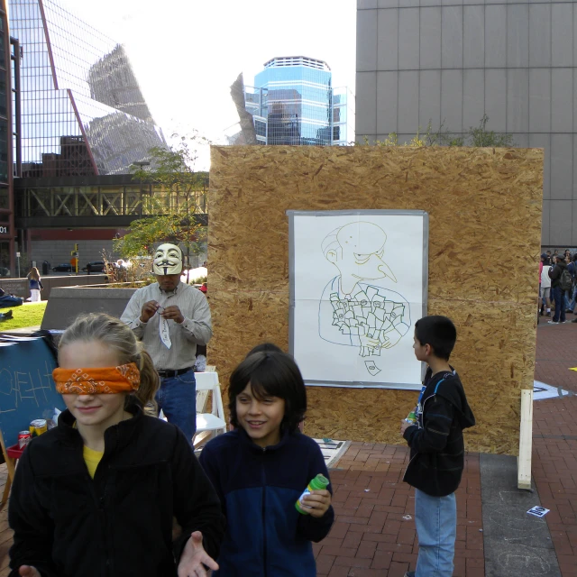 two s in blindfolds stand near a white drawing and a wooden box with an object on it