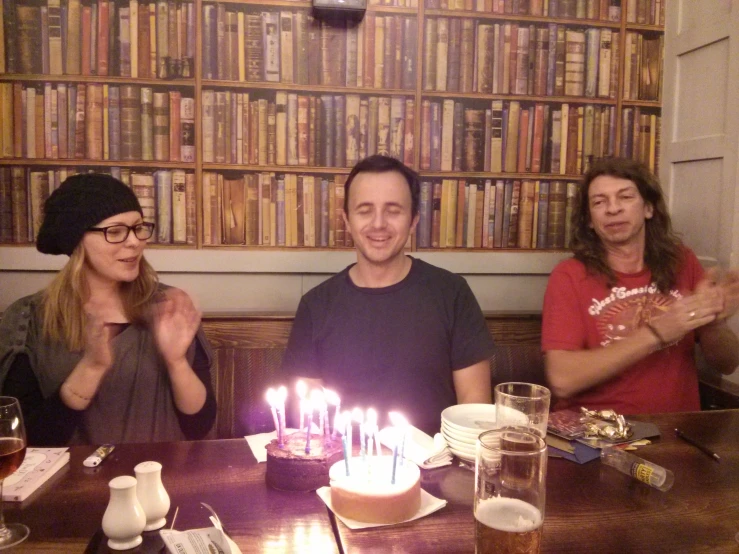 three people seated at a table with a birthday cake