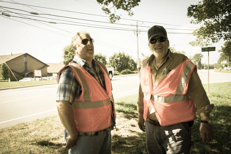 two men standing on a grass covered sidewalk next to the road