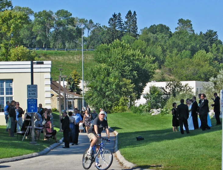 many people standing on the grass near a street with bikes