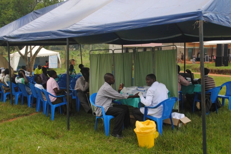 a group of people sitting at blue chairs under a tent