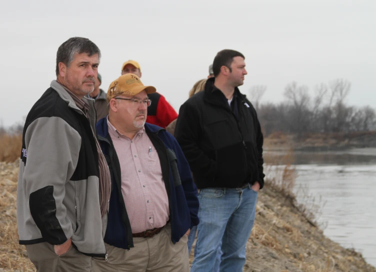 four people standing by the water, some standing looking away