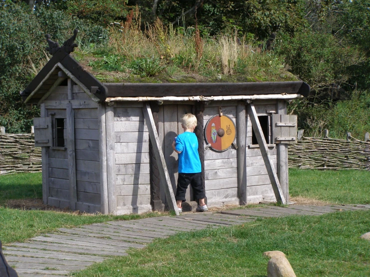 a child in a blue shirt is standing next to a little shack