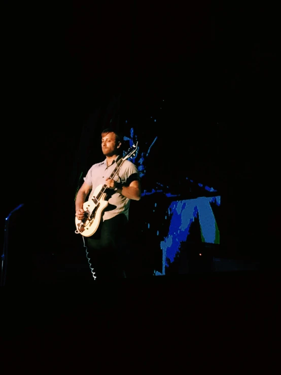 man playing electric guitar on stage at dark time