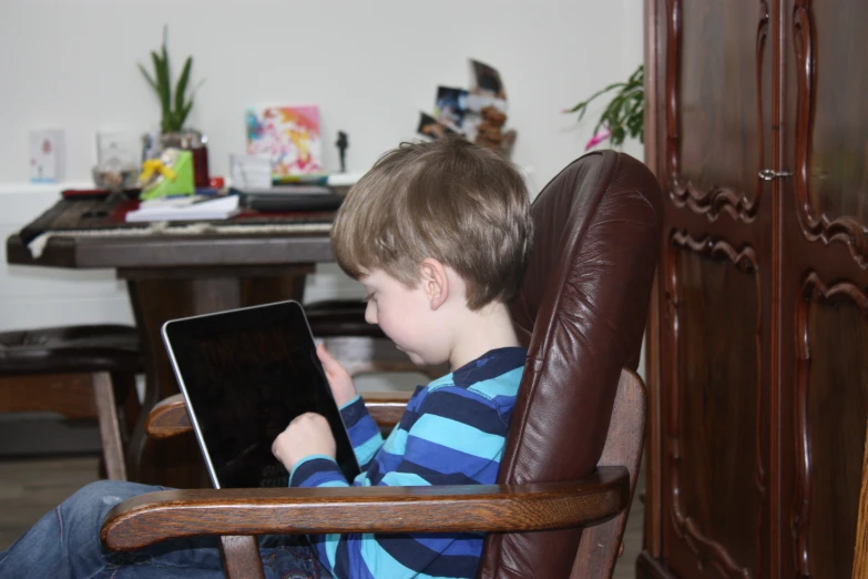a  in blue striped shirt on brown chair looking at a laptop