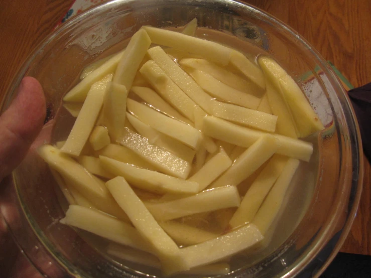 someone holding a clear bowl full of sliced bananas