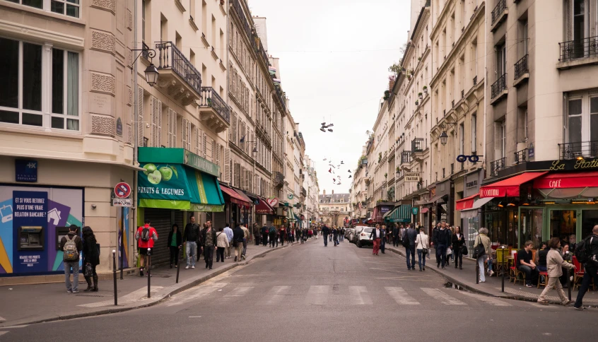 some people are standing on the curb of this narrow city street