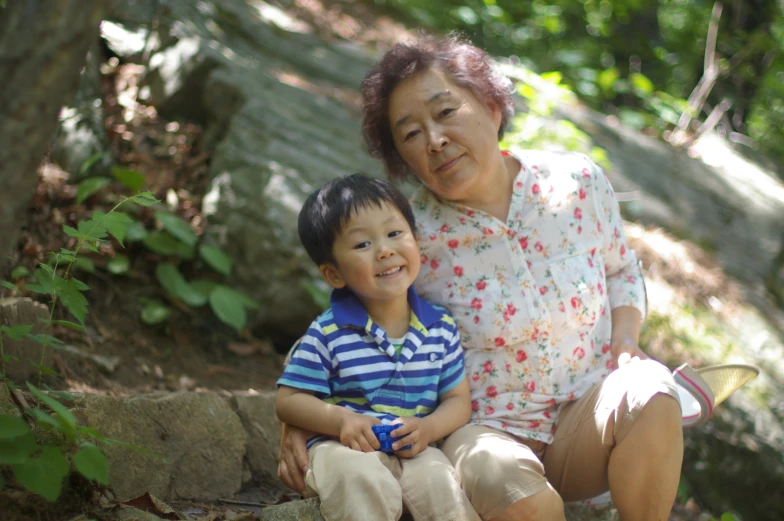 a woman and boy sitting next to each other in the woods