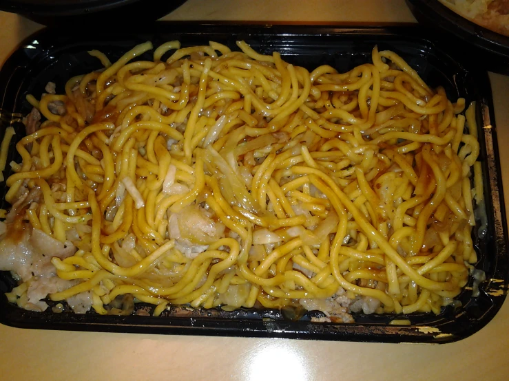 noodles on a black tray is topped with chicken