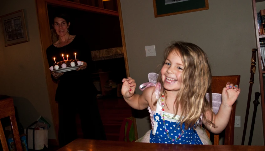 a little girl is sitting at a table and holding some cake