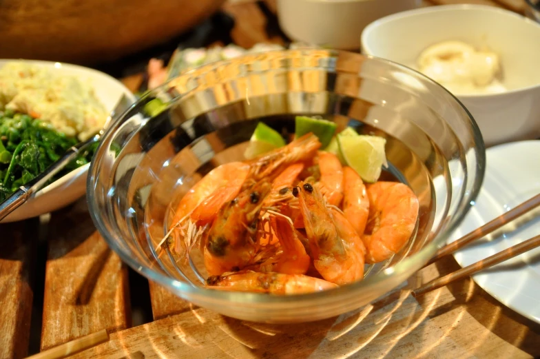 bowl of shrimp with garnishes next to other foods on table