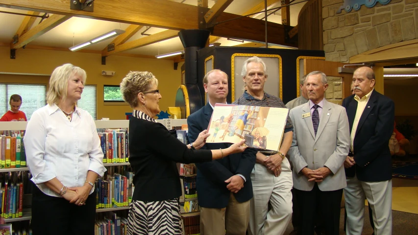 four people stand near a woman and man holding up a painting in a liry