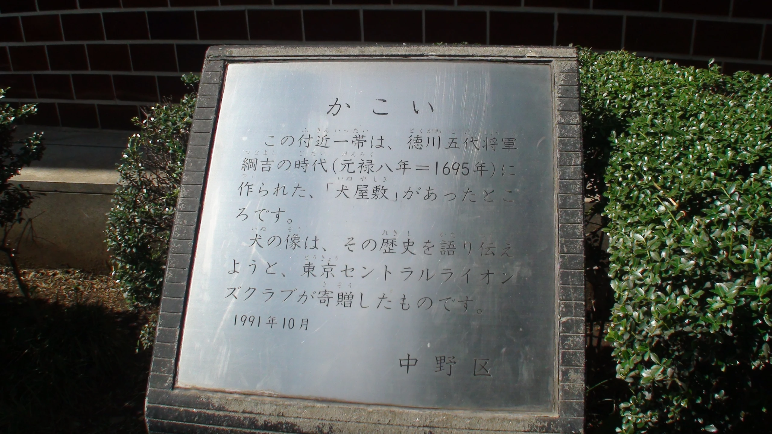 a sign near a hedge on a sidewalk