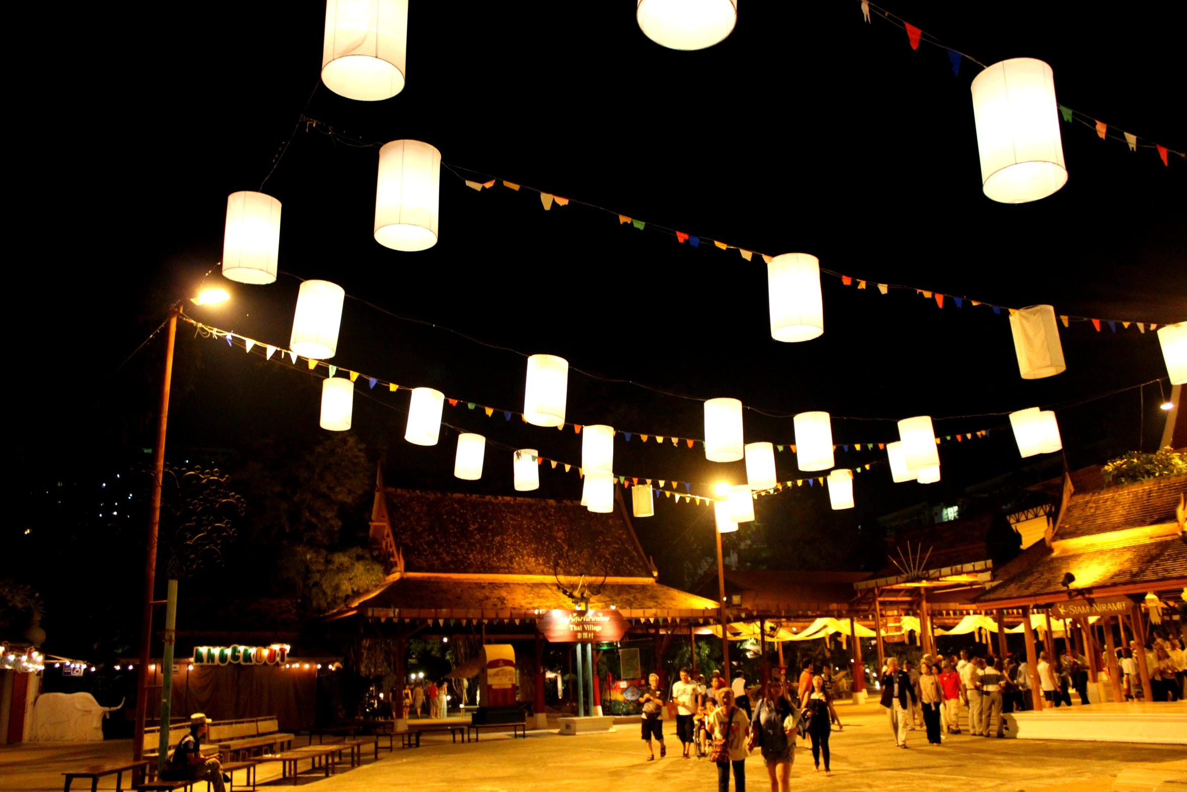 people are walking through the town plaza at night