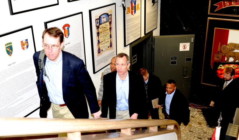 three men in business suits walking up steps near pictures