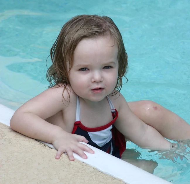 the little girl is sitting in the swimming pool