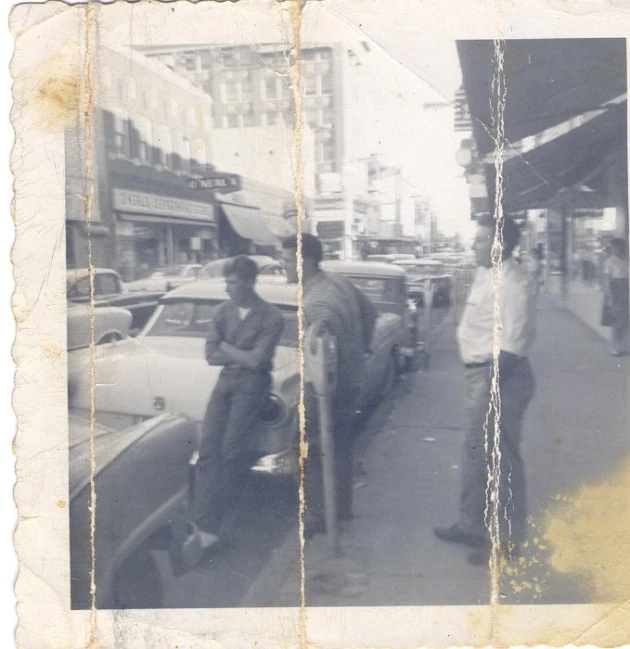 an old black and white pograph of two men standing on a sidewalk