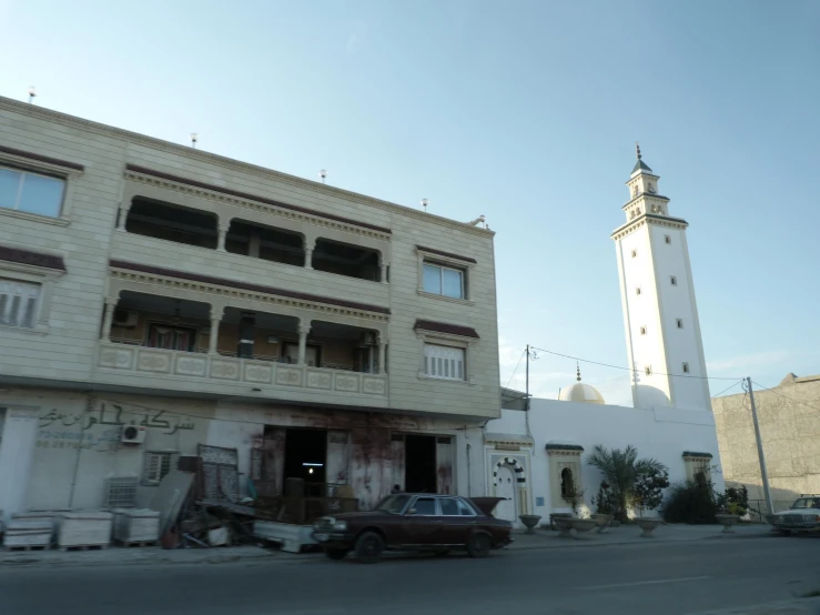 an old car sits parked outside of a building near a clock tower