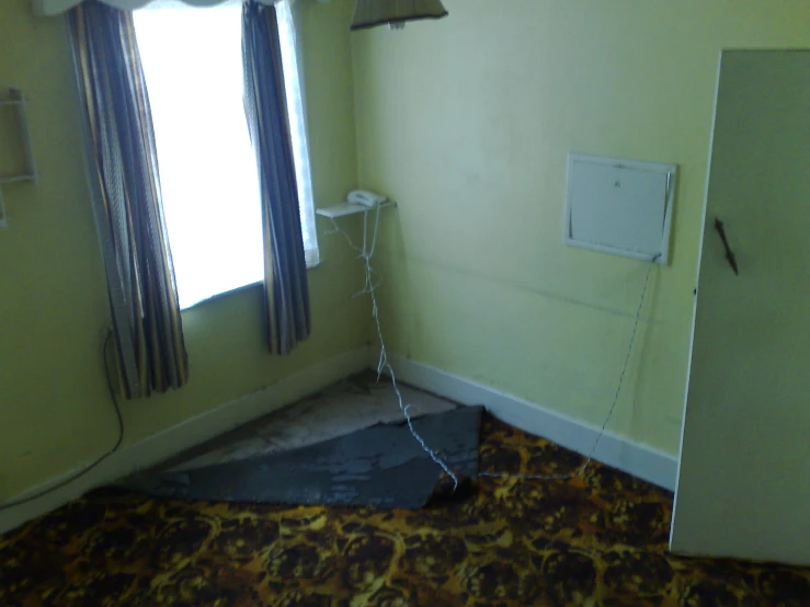 an empty room with a door on the floor, telephone in wall and a curtain with a lock on it